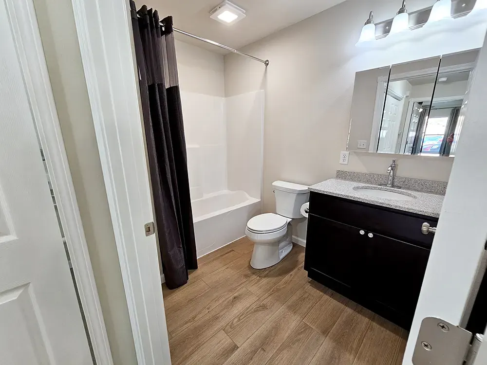 All-new tub/shower, toilet, and espresso quartz-top vanity, set against beautiful luxury vinyl plank flooring.