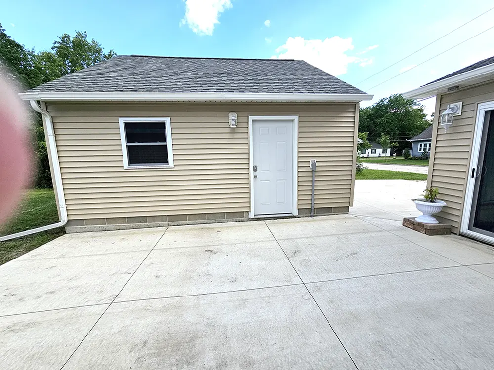 A large, private patio area featuring views of the garage doorway, breezeway, and part of the patio door, with excellent lighting and outdoor electrical outlets ideal for hanging lights.