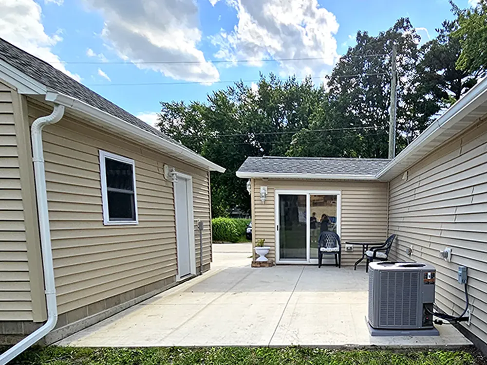 A large, private patio area featuring views of the garage doorway, breezeway, and part of the patio door, with excellent lighting and outdoor electrical outlets ideal for hanging lights.